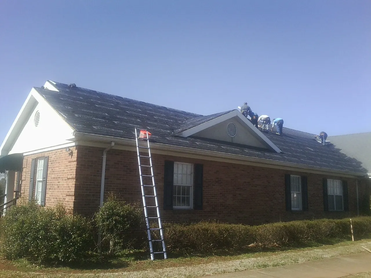Crew tearing shingles off a brick ranch roof with a ladder set — Metal Roof Repair work by our crew in Denmark