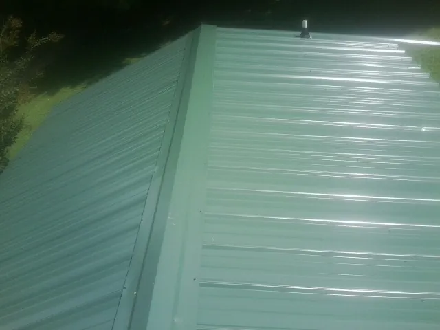 New green metal panels meeting at the ridge of a roof — Flat Roof Repair work by our crew in Denmark